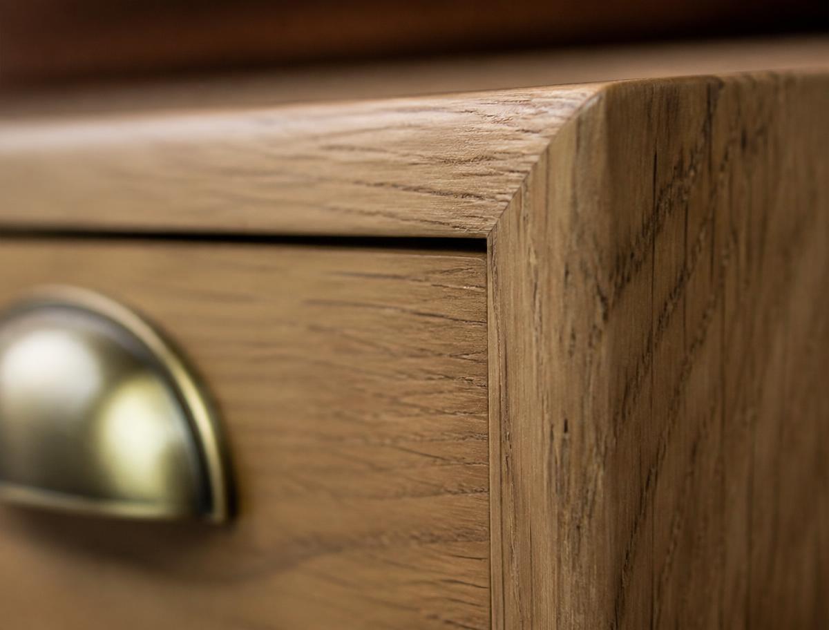 Close detail of an oak drawer front, hand-sanded edge and brass cup pull