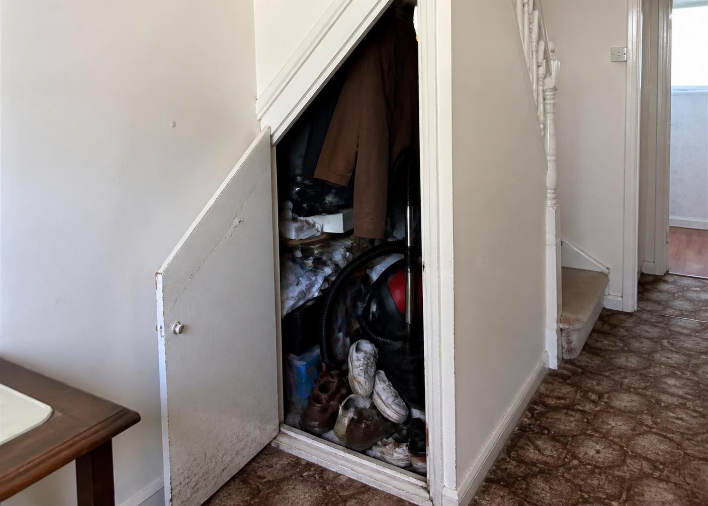 The original cluttered triangular under-stair cupboard before the joinery work